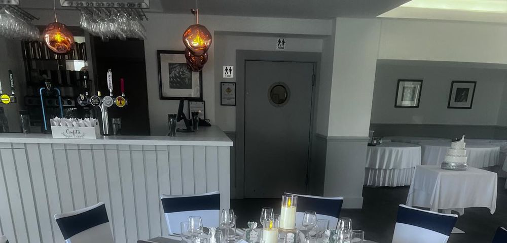 The bar at The Balgarth Pines, taps and glassware along a white panelled counter under copper pendant lights, with the top of a dressed table in the foreground