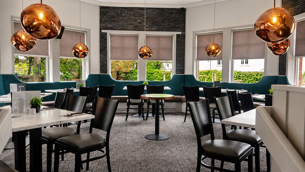 The conservatory at The Balgarth Pines, teal booth seating and marble topped tables under copper pendant lights, with the garden through the windows