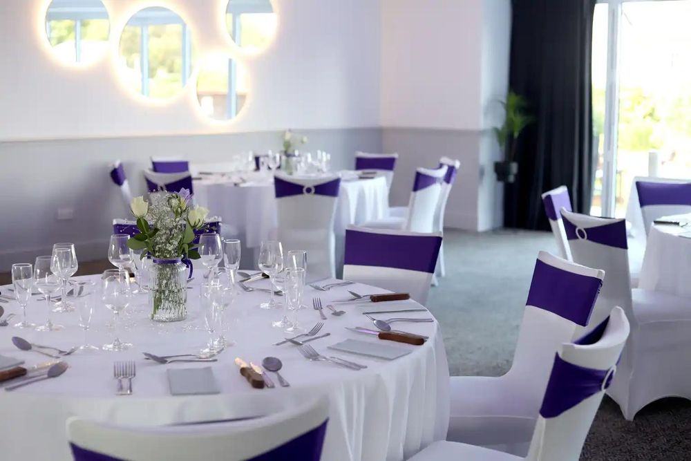 A dressed round table at The Balgarth Pines with a small vase of white roses, under illuminated circular wall mirrors