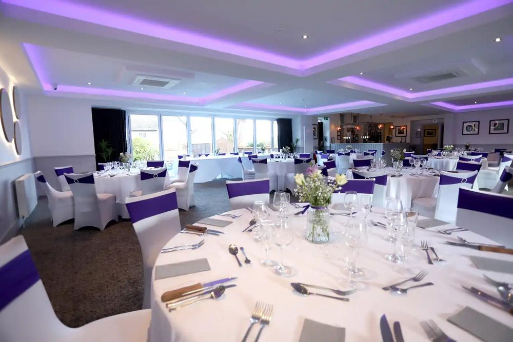The function suite at The Balgarth Pines set with dressed round tables under lilac ceiling lighting, the bar in the distance